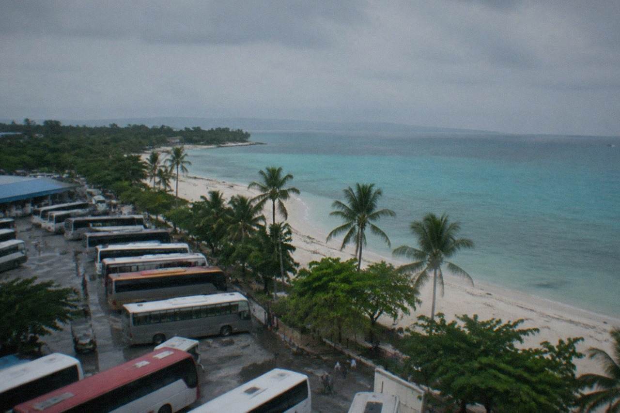 A wide white sand beach with calm turquoise water and a few palm trees along the shore