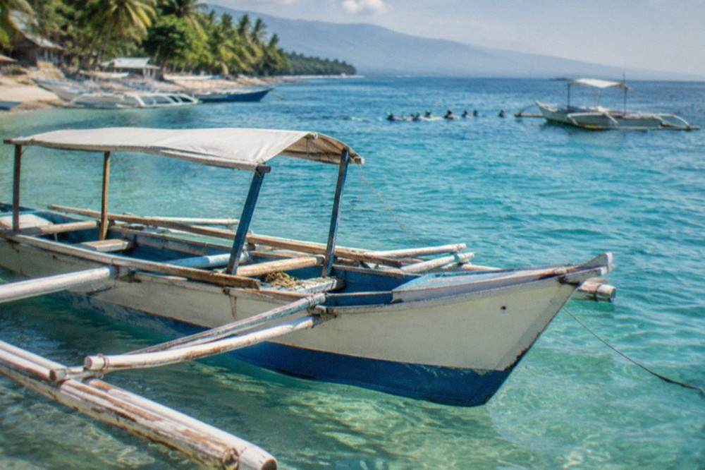 Wooden outrigger boats moored in shallow water along a tropical beach at sunrise