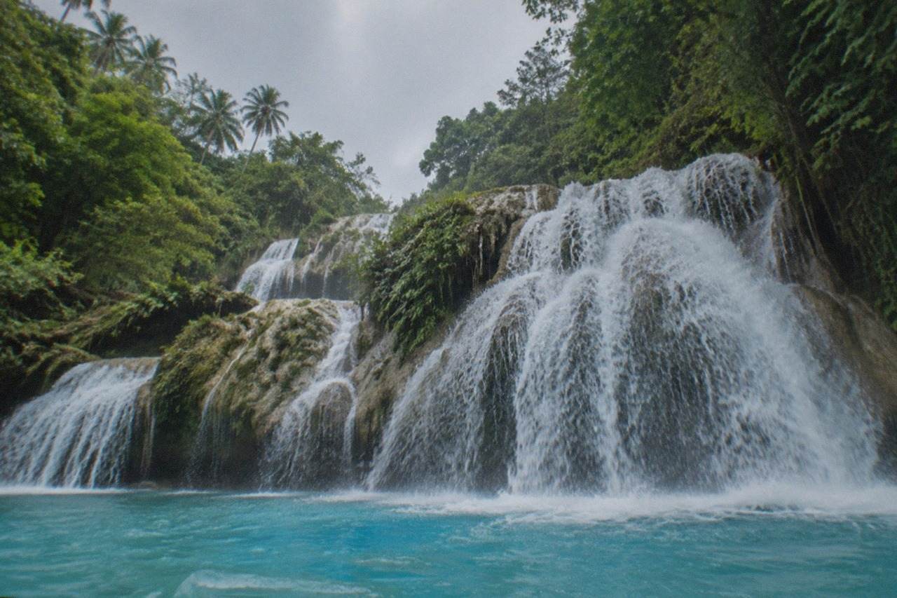 Turquoise water pouring over the wide multi-tiered falls at Kawasan in Badian, Cebu, framed by dense tropical greenery