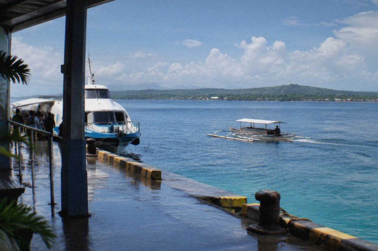 A wooden boat crossing calm blue water between green islands in the Central Visayas, Philippines