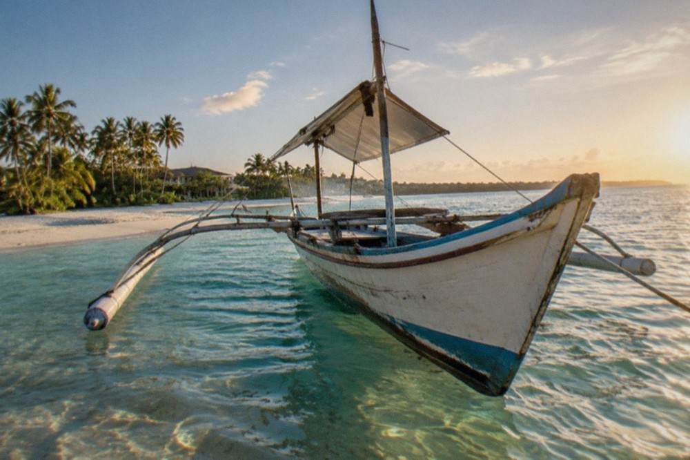 A wooden outrigger boat moored in shallow clear water beside a small sandbank island near Mactan