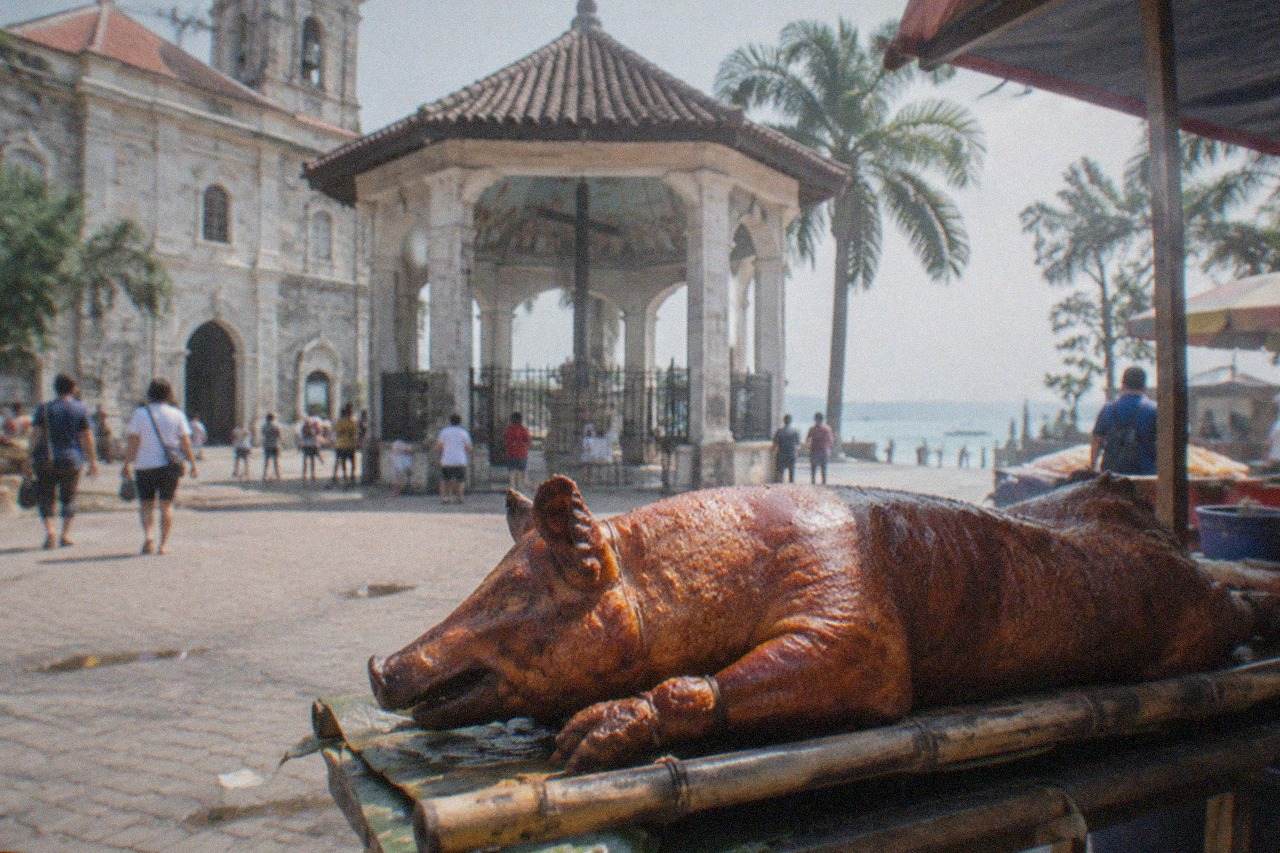 A whole roasted pig with glossy golden-brown crispy skin resting on a bamboo tray at an outdoor Cebu market stall