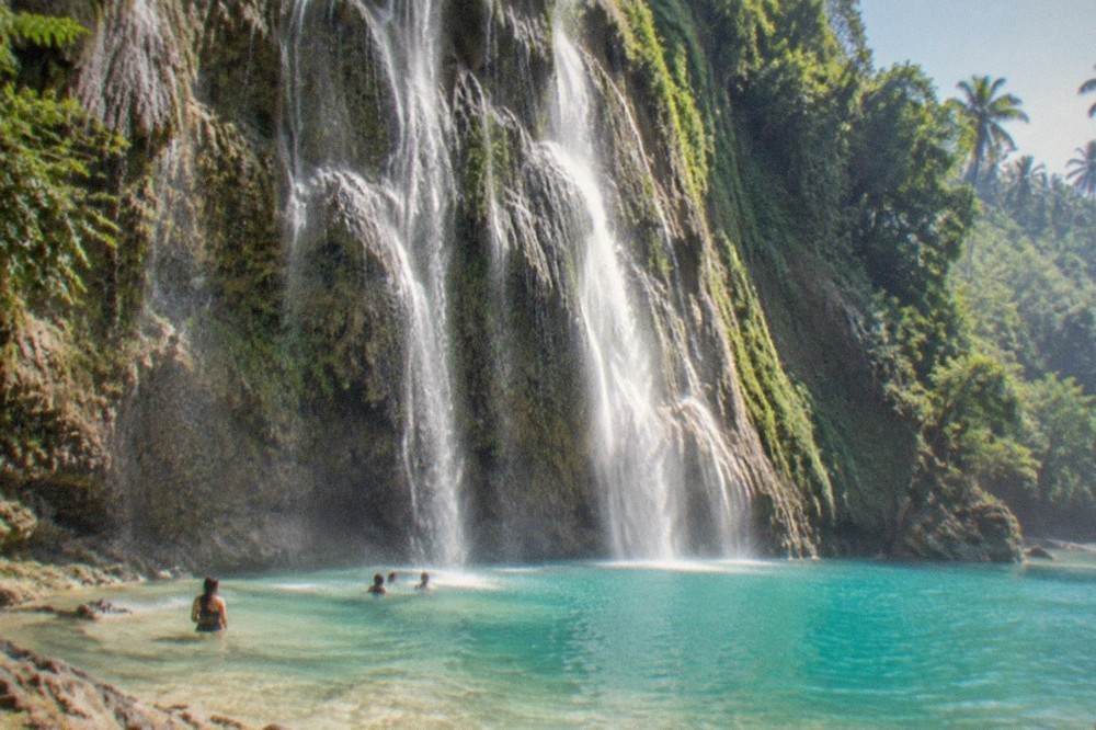 A wide waterfall fanning over a green limestone cliff into a turquoise pool at Tumalog Falls, Oslob