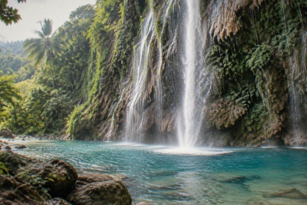 A thin ribbon waterfall dropping into a turquoise pool at Tumalog Falls near Oslob, Cebu
