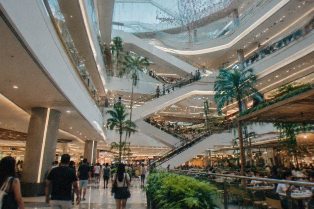 Shoppers walking through a bright multi-level mall atrium with restaurants and escalators