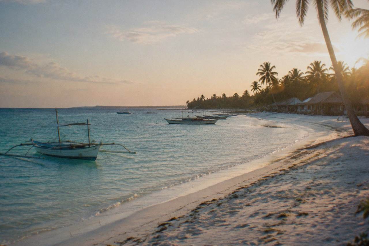 A quiet white sand beach on Bantayan Island with calm shallow water and a few fishing boats along the shore
