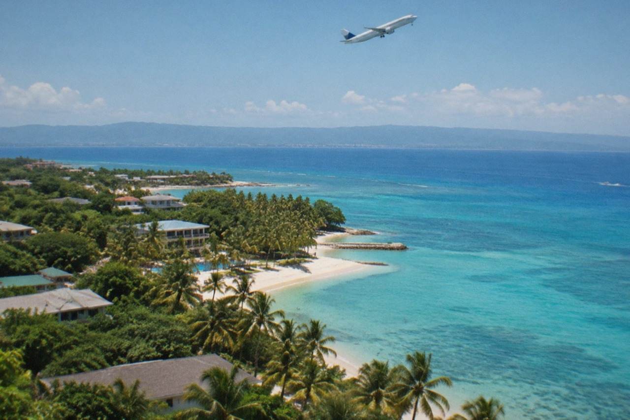 A passenger airplane climbing above the coastline of Mactan island near Cebu, with calm sea and distant hills.
