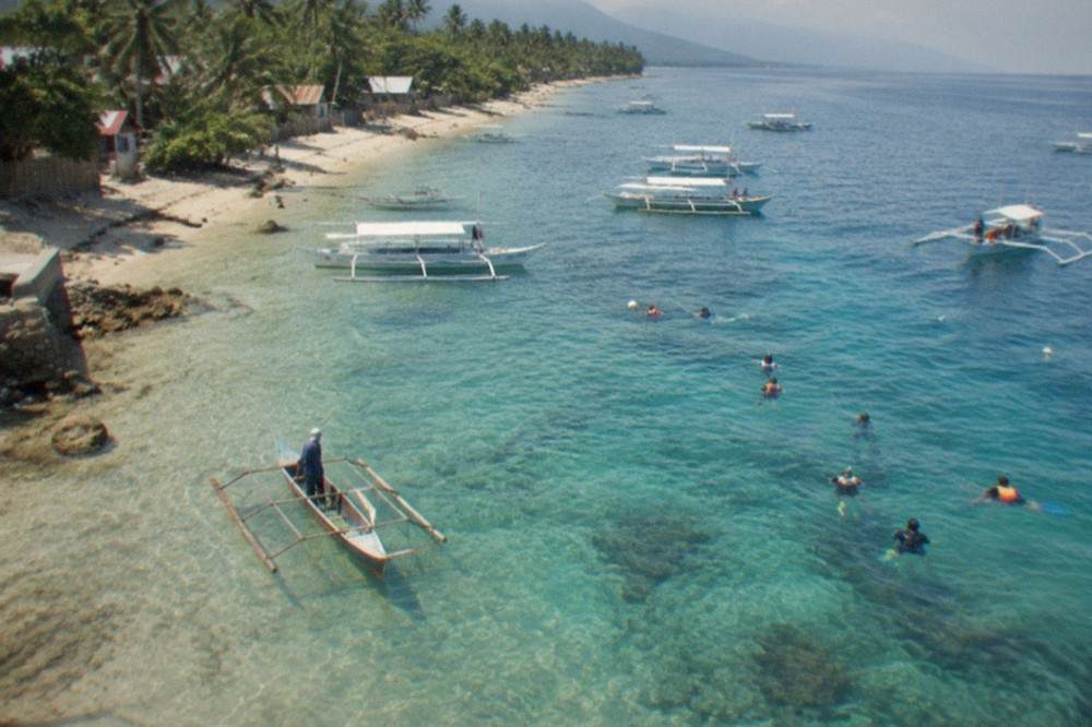 A wooden paddle boat and guide waiting near the shoreline at the Oslob whale shark briefing area