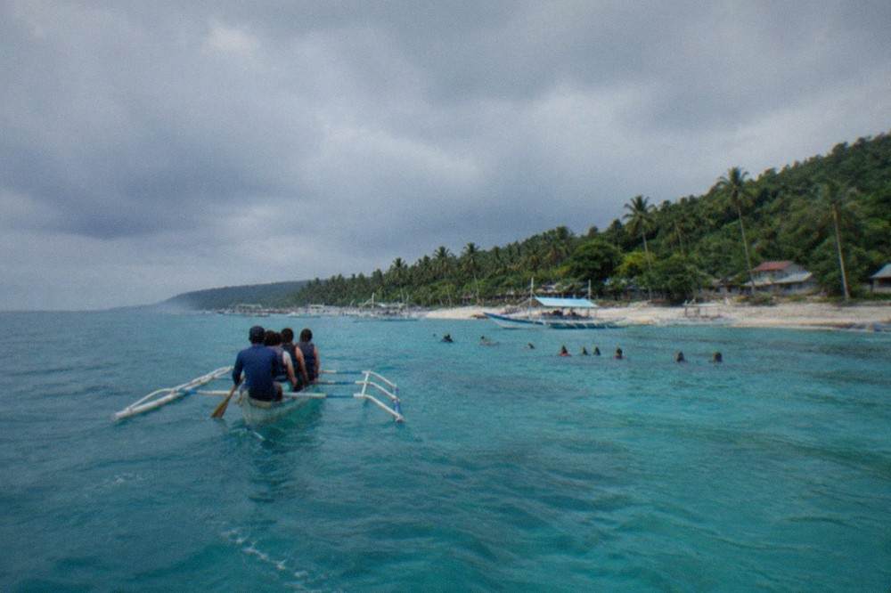A wooden paddle boat carrying visitors out over shallow water toward the whale shark interaction area in Oslob