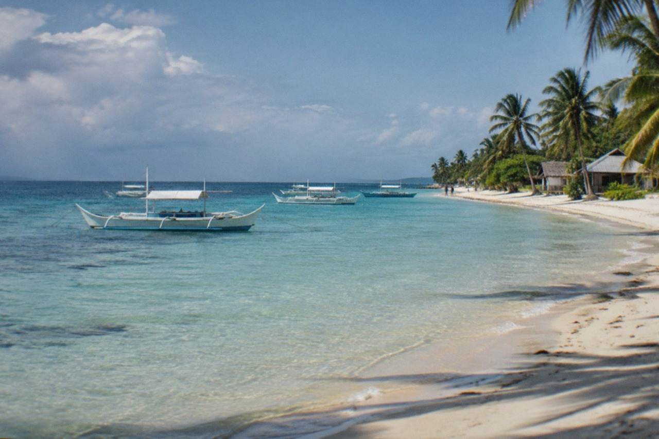 A quiet white sand beach on Bantayan Island with calm shallow water and a few outrigger boats at anchor