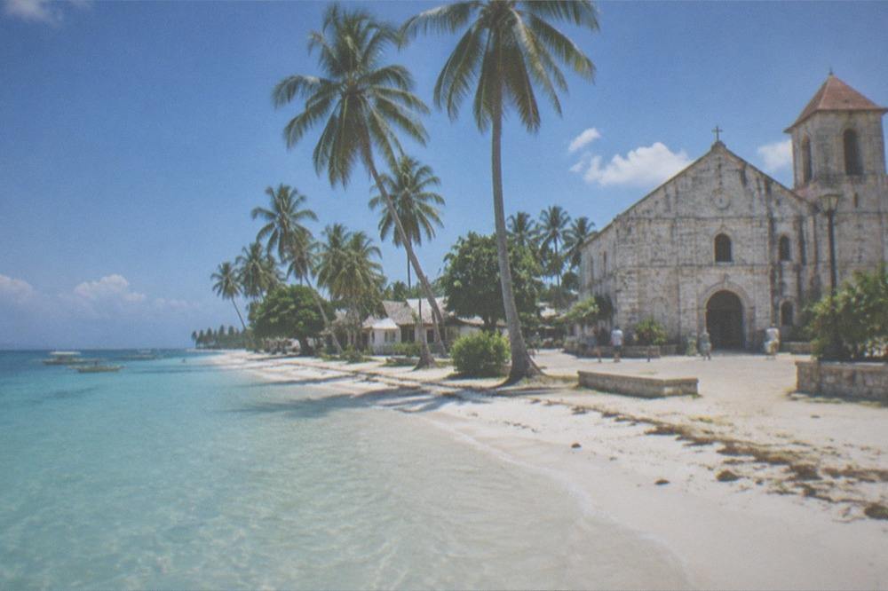 A coral stone church facade in a small town square on Bantayan Island under an afternoon sky