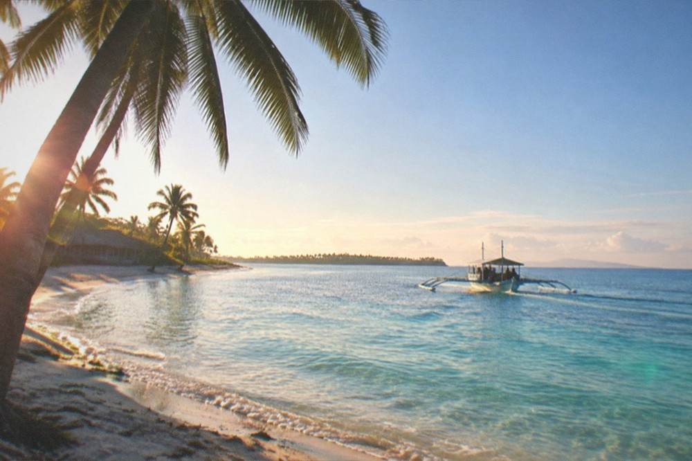 An outrigger ferry boat crossing calm blue water toward Bantayan Island in early morning light