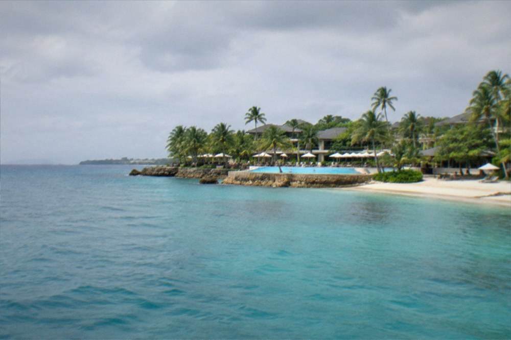 A resort swimming pool and beach on Mactan Island seen across calm water