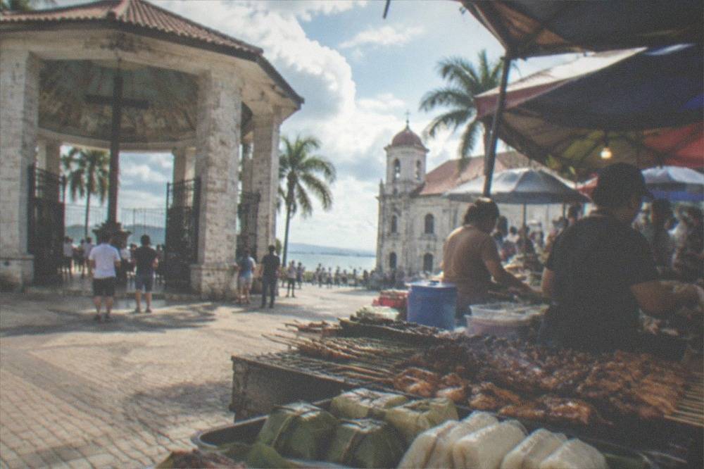 A crowded Cebu public market stall with grilled meats, rice parcels and vendors serving customers