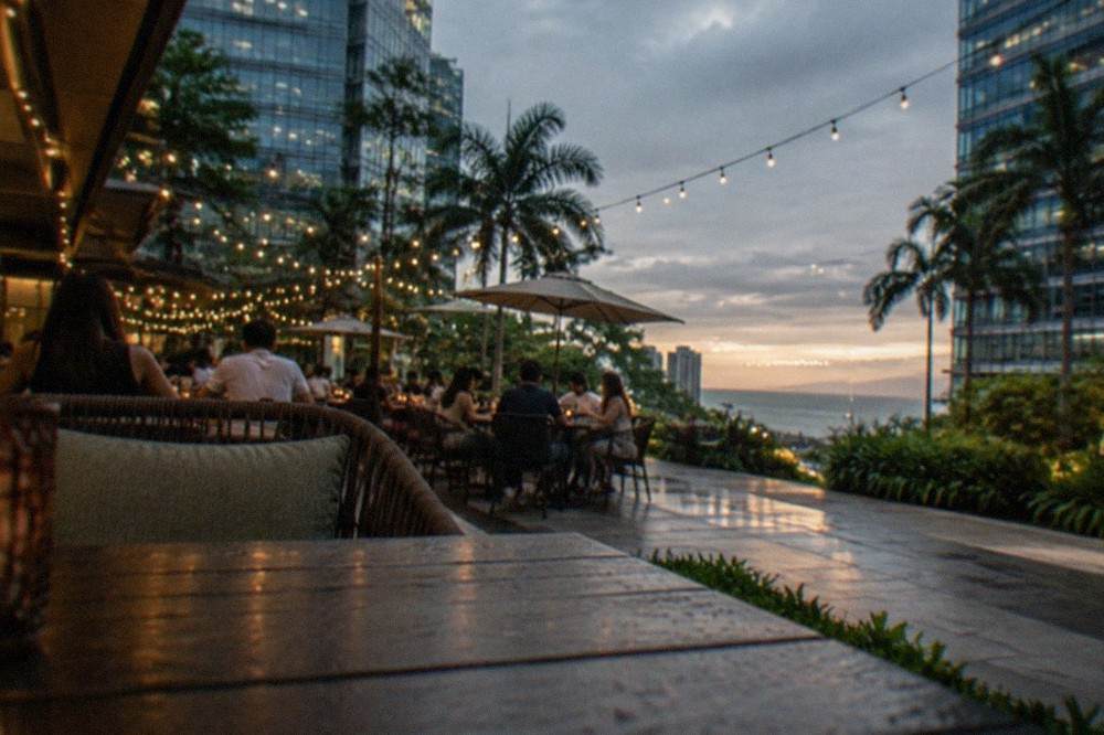 People dining at outdoor tables under string lights in a courtyard restaurant area at dusk