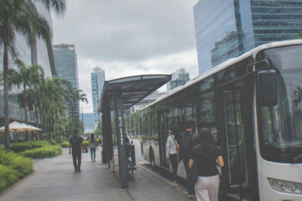 An air-conditioned city bus pulling into a sheltered stop with passengers boarding