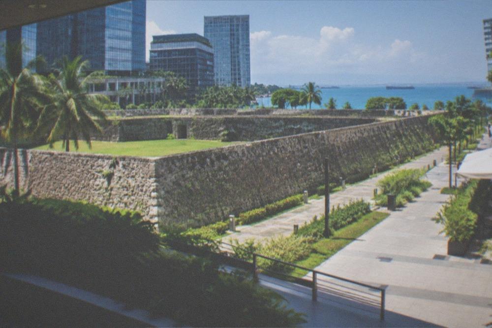 A coral-stone fort with triangular walls and a grassy inner courtyard under a bright sky