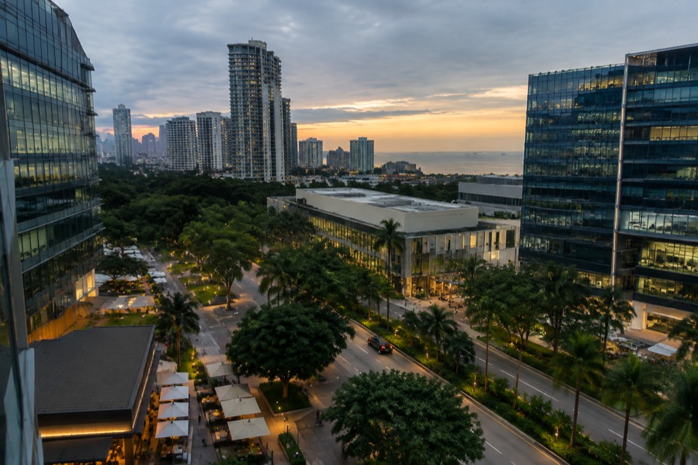 A high-rise residential and hotel skyline glowing at dusk above a business district plaza