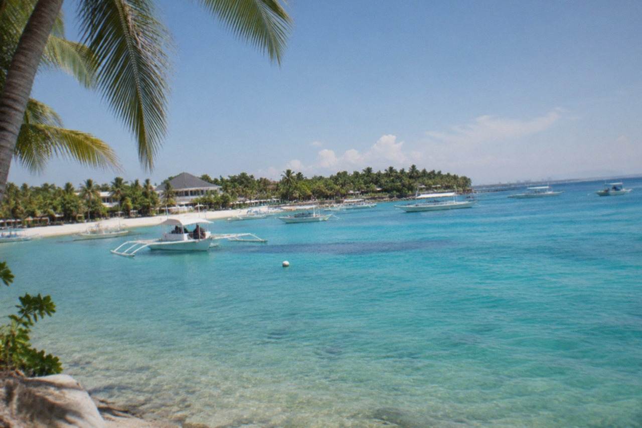 A view across the water toward Mactan Island with boats moored near a beach