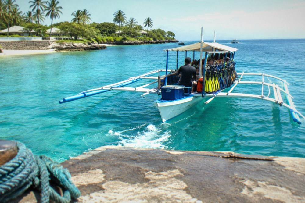 A small outrigger boat loaded with snorkel gear leaving a jetty for island hopping