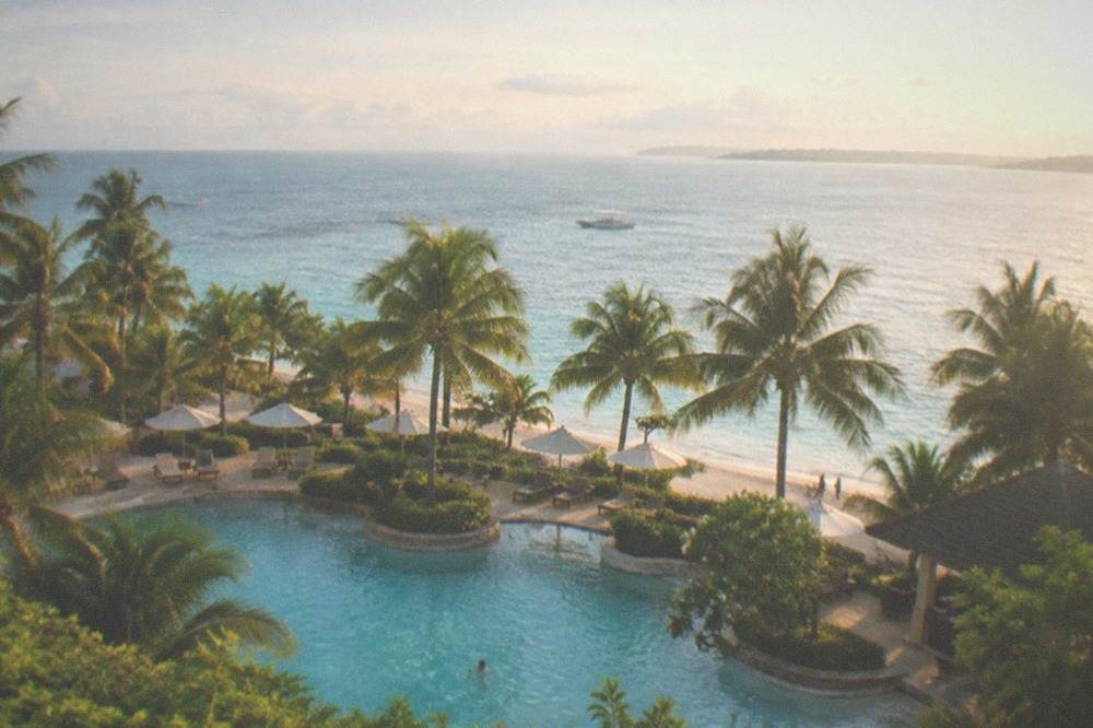 A resort swimming pool and palm trees beside a calm sea at late afternoon