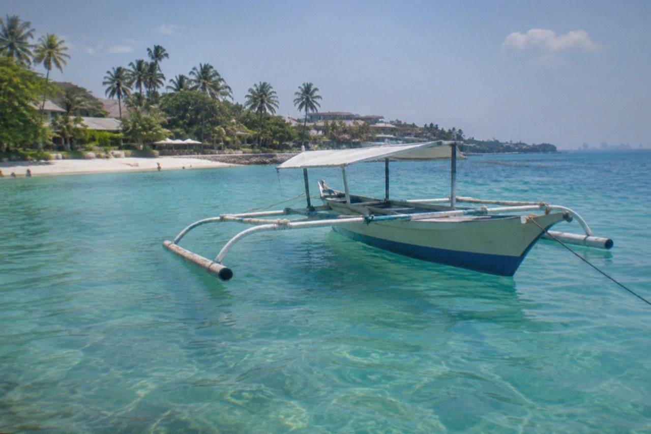 A wooden outrigger boat anchored in clear turquoise water off a tropical island beach