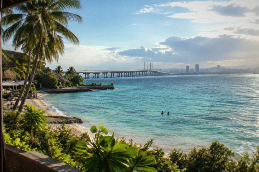 A long sea bridge crossing a channel toward a city skyline in late afternoon light