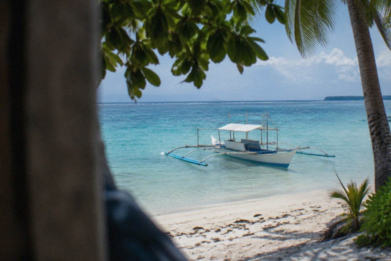 A small outrigger boat resting in shallow turquoise water beside a tropical island beach
