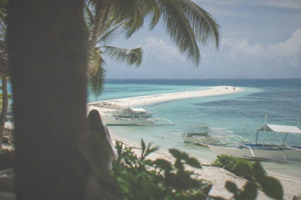 A long white sandbar stretching into calm turquoise sea under a bright sky