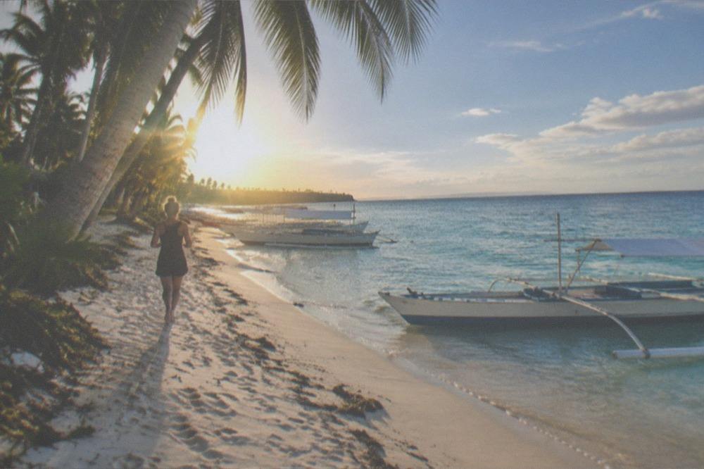 Palm trees leaning over a quiet tropical beach under scattered clouds