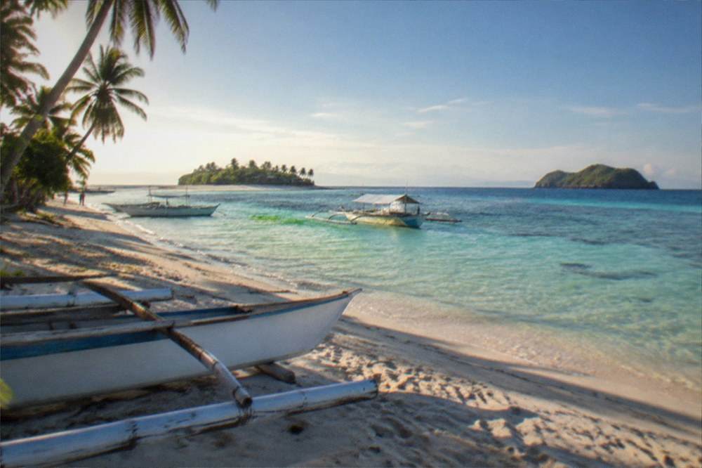 Two islands seen from the water, one with a sandy shoreline and green palms