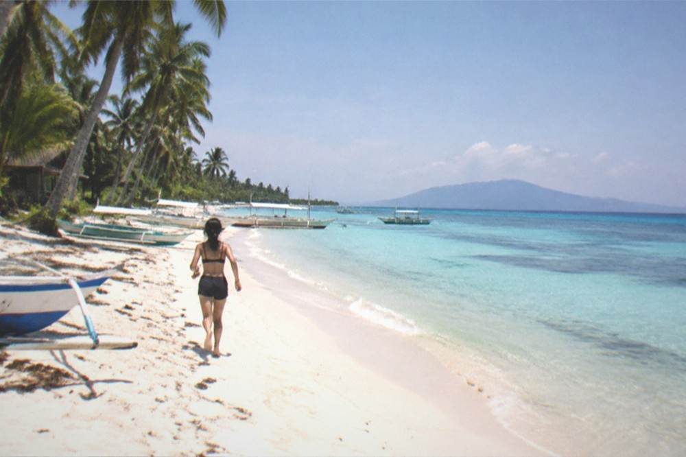 A quiet tropical beach at first light with calm water and a distant island silhouette