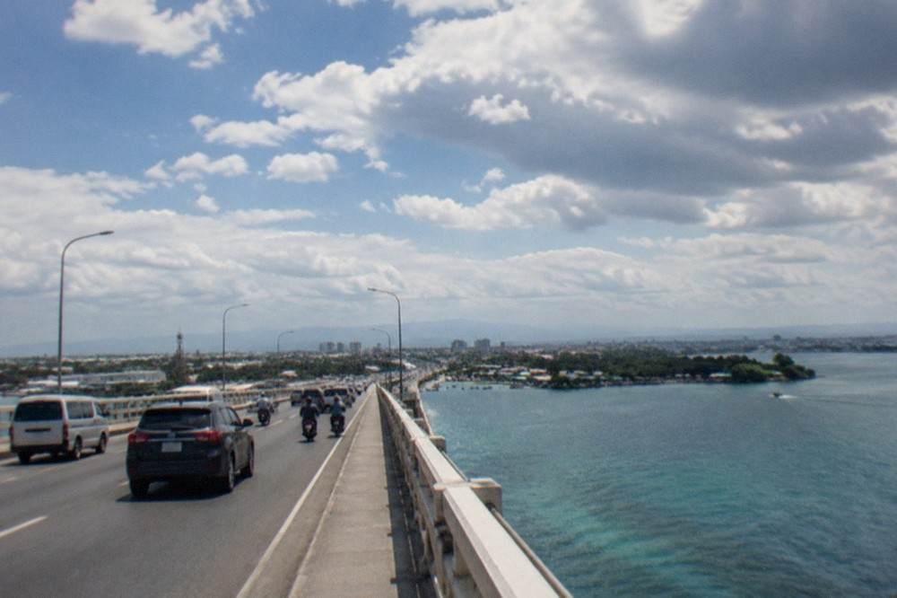 Traffic crossing a long bridge over the Mactan Channel toward Mactan island at midday