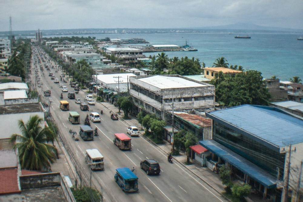 Jeepneys and cars on a wide avenue in Mandaue with commercial buildings on both sides