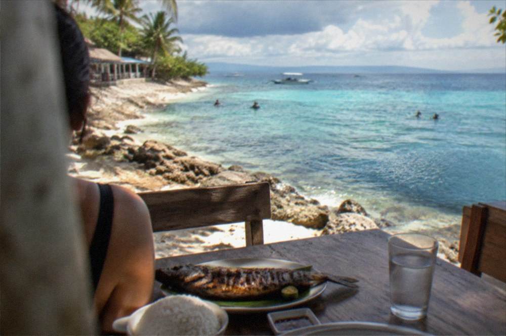 A grilled fish dinner and rice served at a simple wooden beachside table