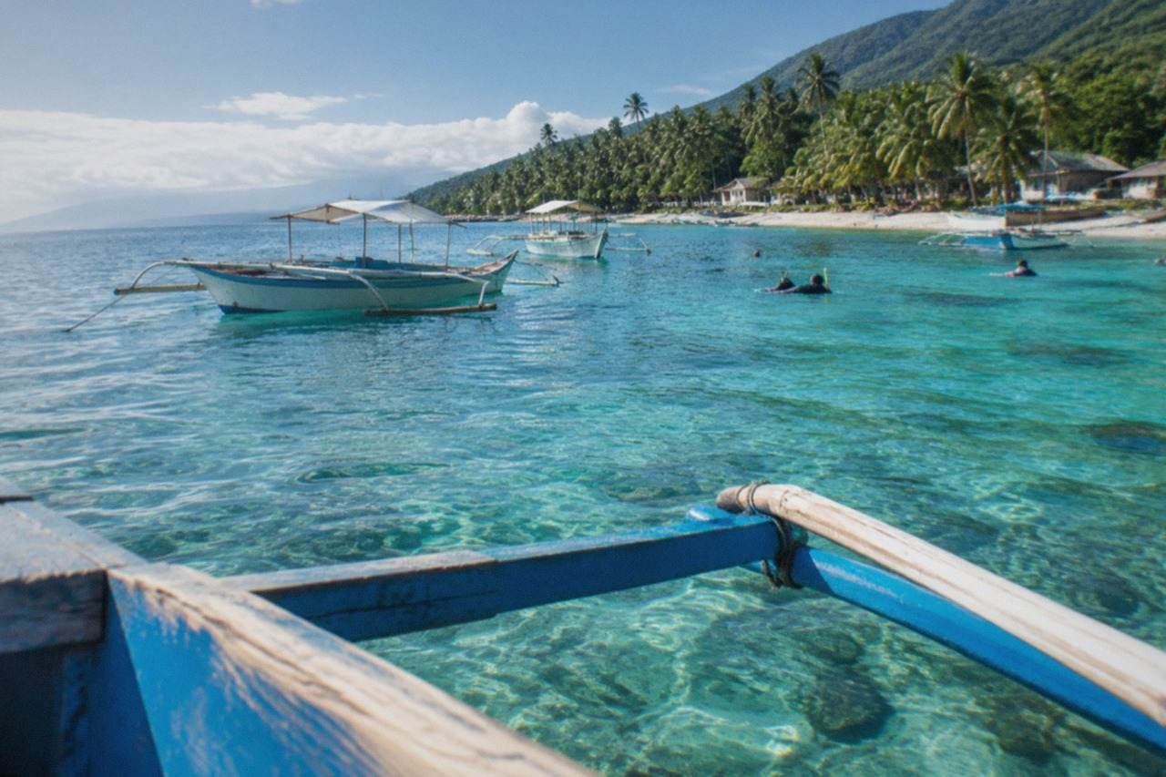 Wooden outrigger boats floating on clear turquoise water off a tropical Philippine coastline in the morning