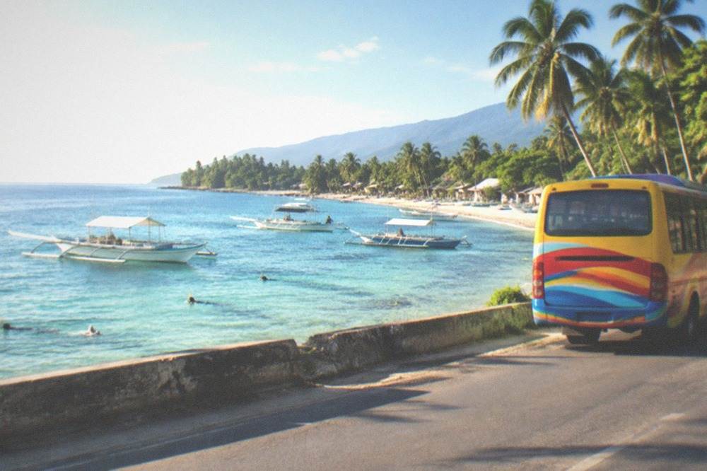 A colourful Philippine provincial bus travelling along a coastal road with palm trees and sea views