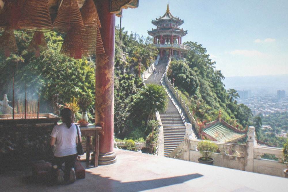 A worshipper kneeling before an altar with burning incense coils hanging overhead