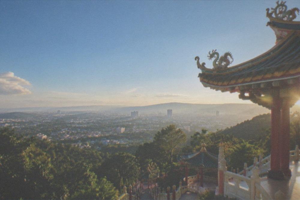 A temple roof detail against a clear blue sky with Cebu City visible below