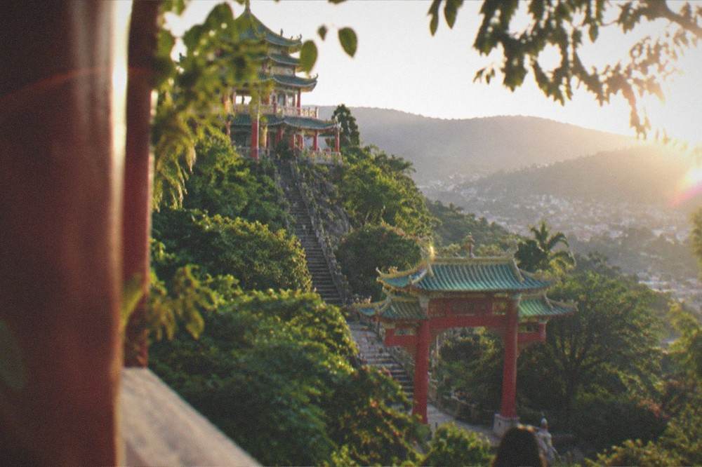 A red temple gate framed by trees with hills rising behind it