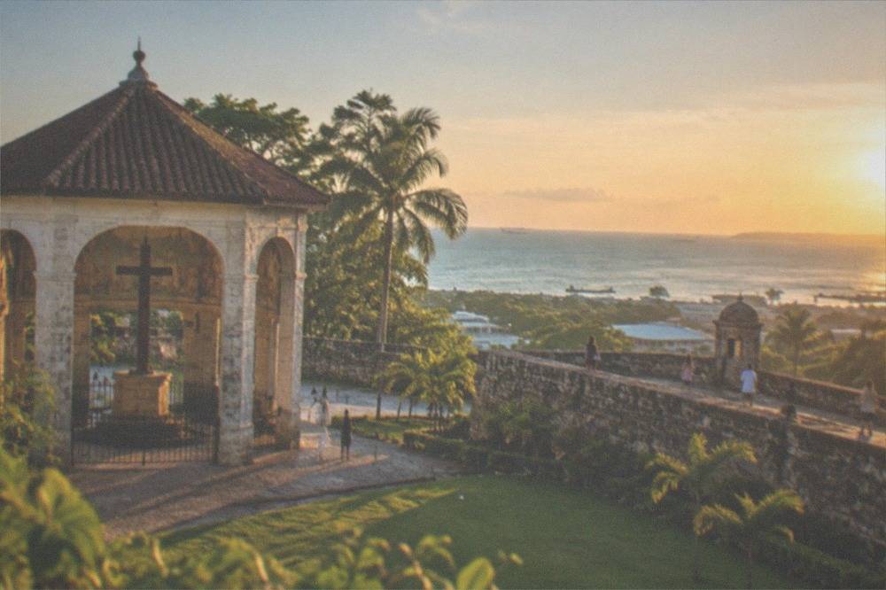 Visitors walking along the rampart of a coral stone fort above a green lawn in Cebu City