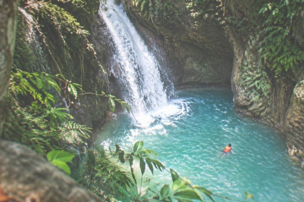 Swimmer in a life vest floating in a blue cascade pool inside a narrow canyon