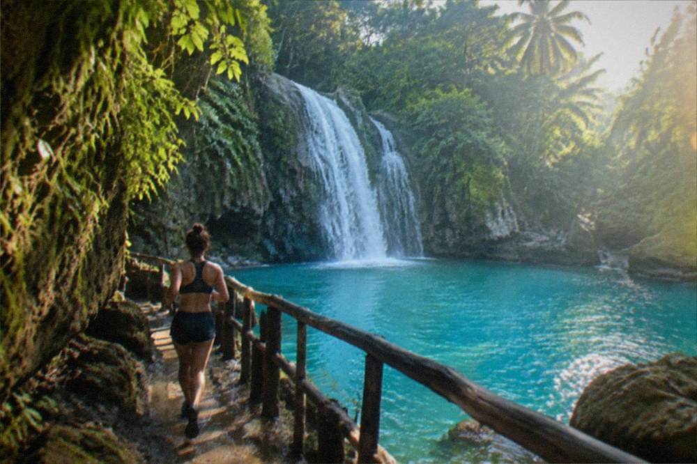 Waterfall cascading into a deep blue pool with wooden railings and jungle cover