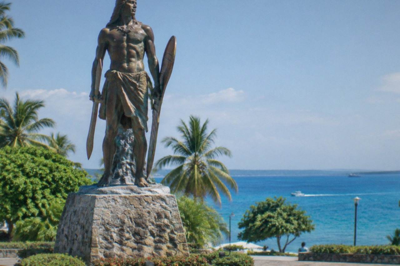 A large bronze statue of a Filipino warrior holding a bolo, standing on a stone platform in a seaside park