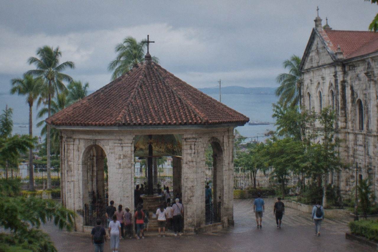 The open-sided stone pavilion housing Magellan's Cross, with the wooden cross visible inside and visitors gathered at the entrance in downtown Cebu City