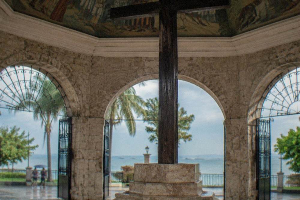 A close view of the dark wooden shaft of Magellan's Cross resting on its raised stone base inside the pavilion
