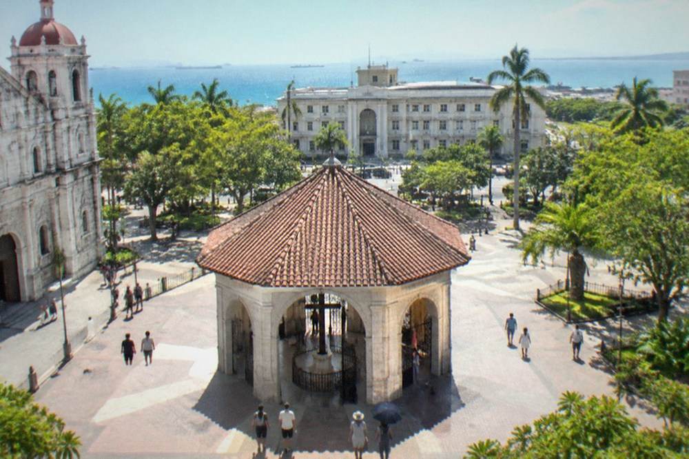 The plaza around Magellan's Cross with pedestrians and the Cebu City Hall building in the background