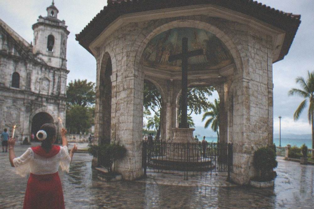An older woman dancing the Sinulog prayer dance with lighted candles near the entrance of the Magellan's Cross pavilion