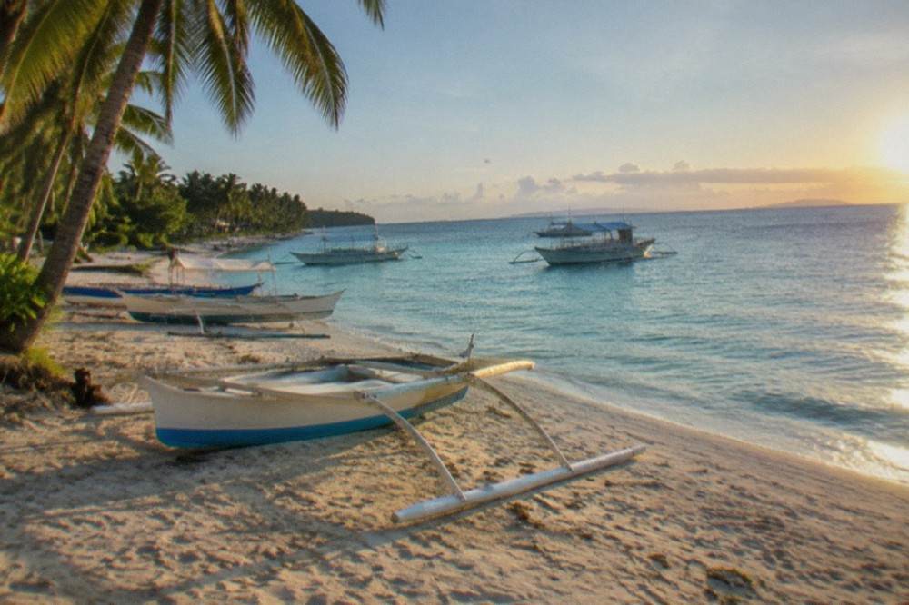 Dive boats moored on a white sand beach at Malapascua Island at first light