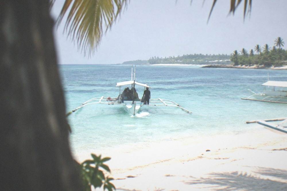 A small outrigger boat arriving at a sandy beach with palm trees on Malapascua Island